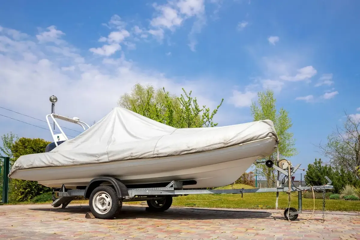 A boat sits covered in a durable wrap while parked on a brick patio with a bright blue sky and clouds.